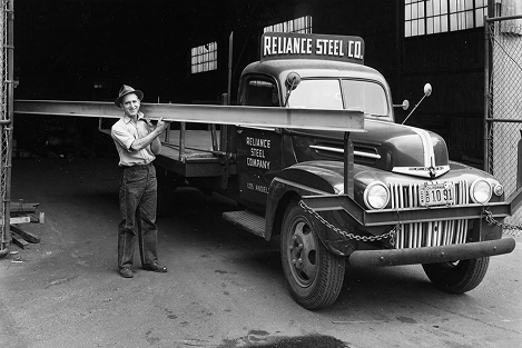 Worker holds a steel beam beside a Reliance Steel Company truck in Los Angeles.