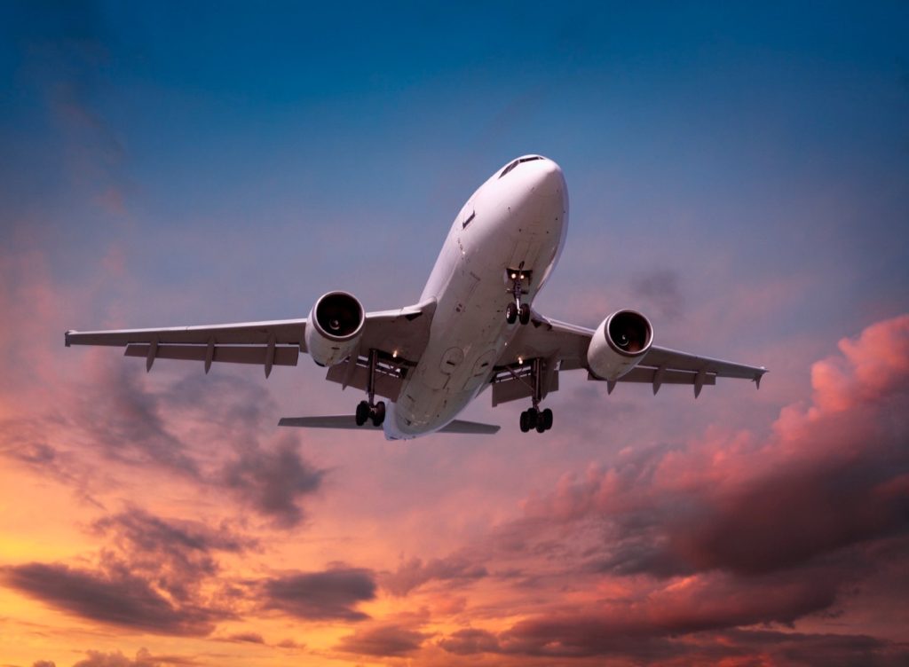 Commercial airplane descends for landing against a colorful sunset sky.