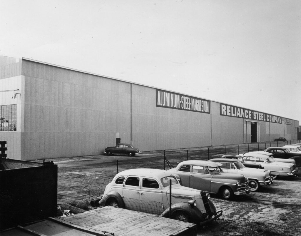 Historic exterior of a Reliance Steel Company building with parked cars.