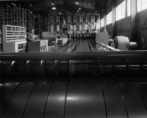 Black-and-white view of a steel slitting line processing wide metal coils.