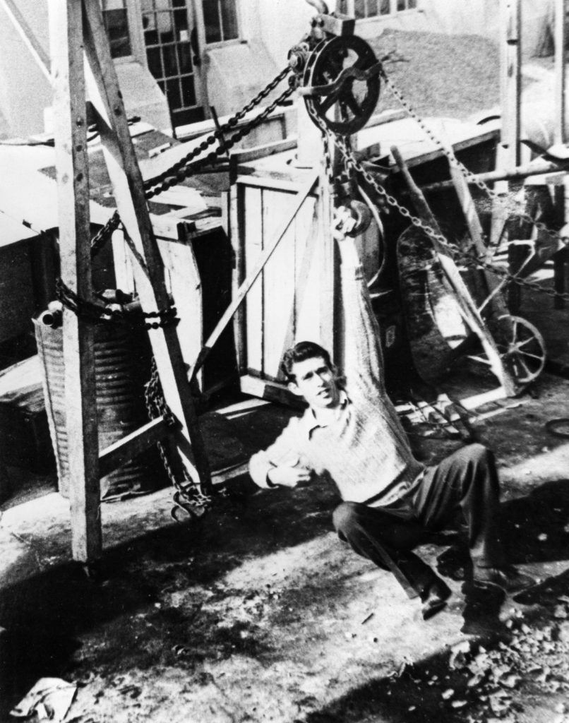 Young man sits beside early workshop equipment in a historic Reliance photo.
