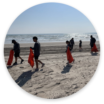 Volunteers walking along a beach carrying orange trash bags during a cleanup.
